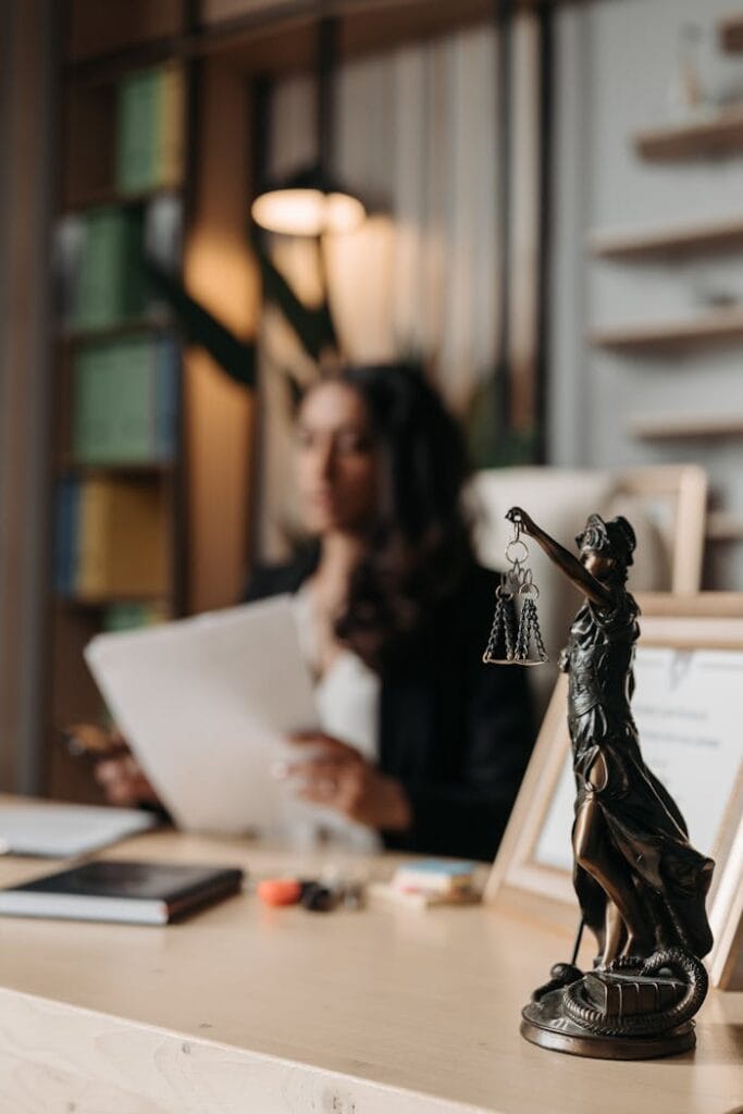 pexels-photo-8111815 Close-up of a justice figurine on desk with blurred female lawyer in office setting.