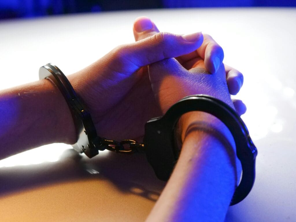 pexels-photo-7773266-7773266 Close-up of handcuffed hands under blue police light, signifying arrest or detention.