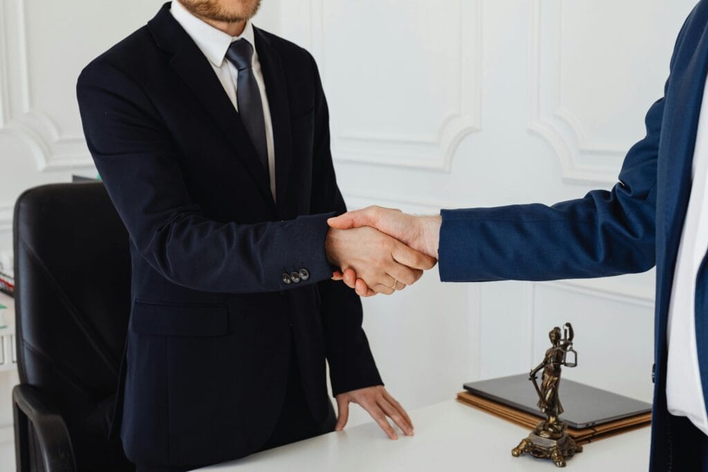 pexels-photo-7875996-7875996 Two men in suits shaking hands in a formal office environment symbolizing an agreement.