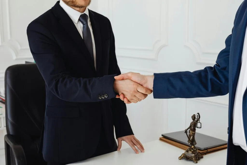 pexels-photo-7875996-7875996 Two men in suits shaking hands in a formal office environment symbolizing an agreement.